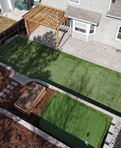 Aerial view of a backyard with turf, a putting green, paver patio and wood pergola.