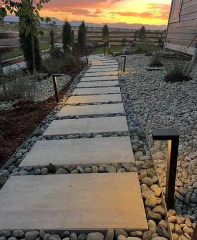 Large rectangular walkway slabs in river rock with illuminated path lights at sunset.