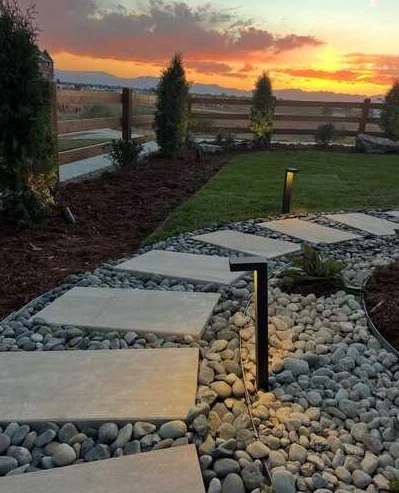 Curved slab walkway through river rock and planting beds with warm path lights.